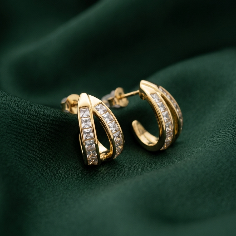 Gold hoop earrings with pavé-set clear stones, displayed on a dark green satin fabric background.