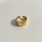 Wide gold ring with geometric basket weave texture standing on white surface.