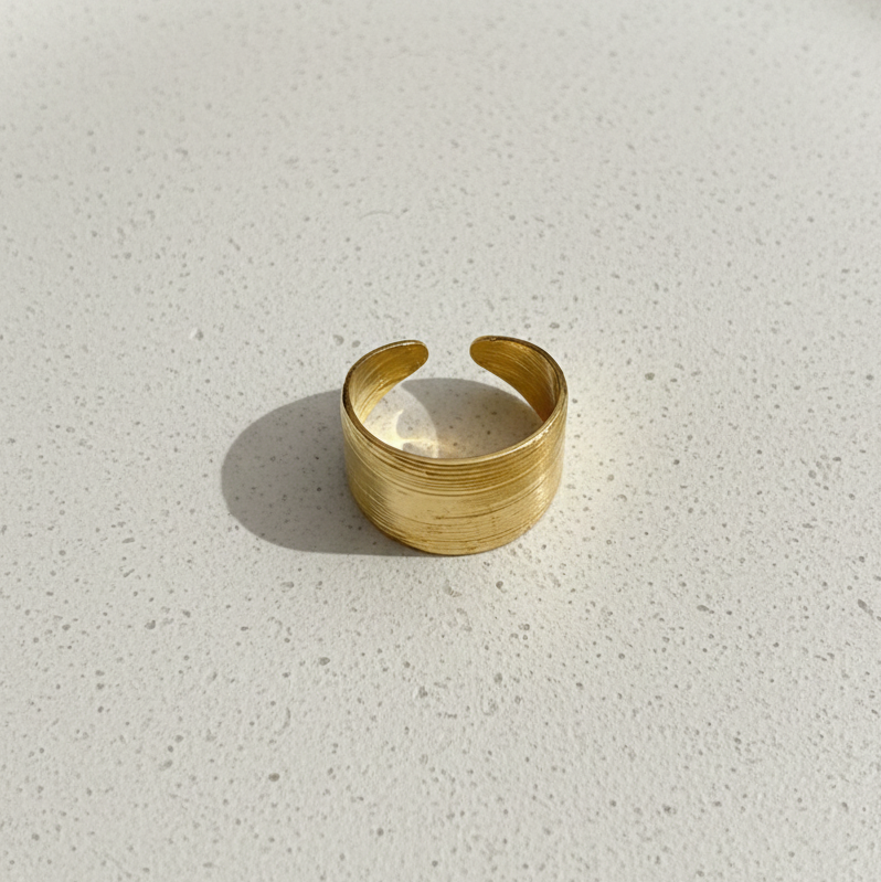 Wide gold ring with geometric basket weave texture standing on white surface.