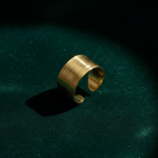 Wide gold ring with geometric basket weave texture standing on white surface.