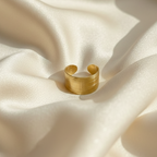 Wide gold ring with geometric basket weave texture standing on white surface.