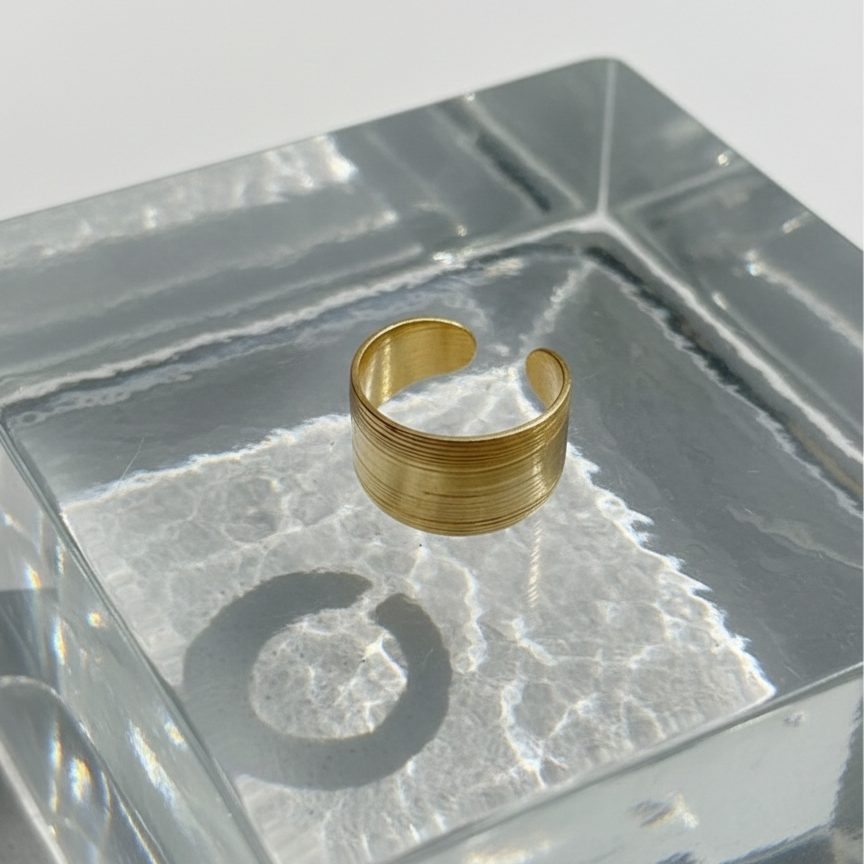 Wide gold ring with geometric basket weave texture standing on white surface.