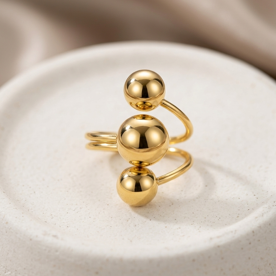 18kt gold plated ring with three polished metal balls in orbit design on white background.