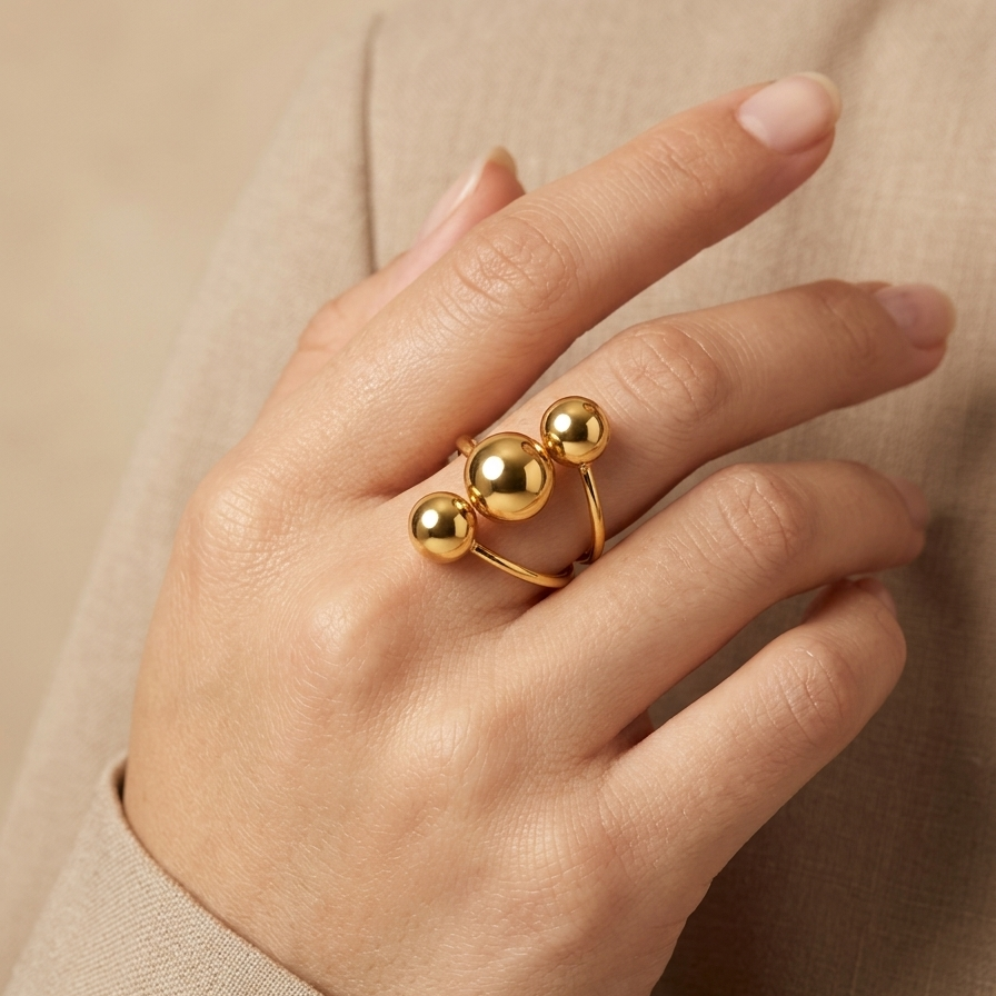 18kt gold plated ring with three spherical beads on a hand against a beige background
