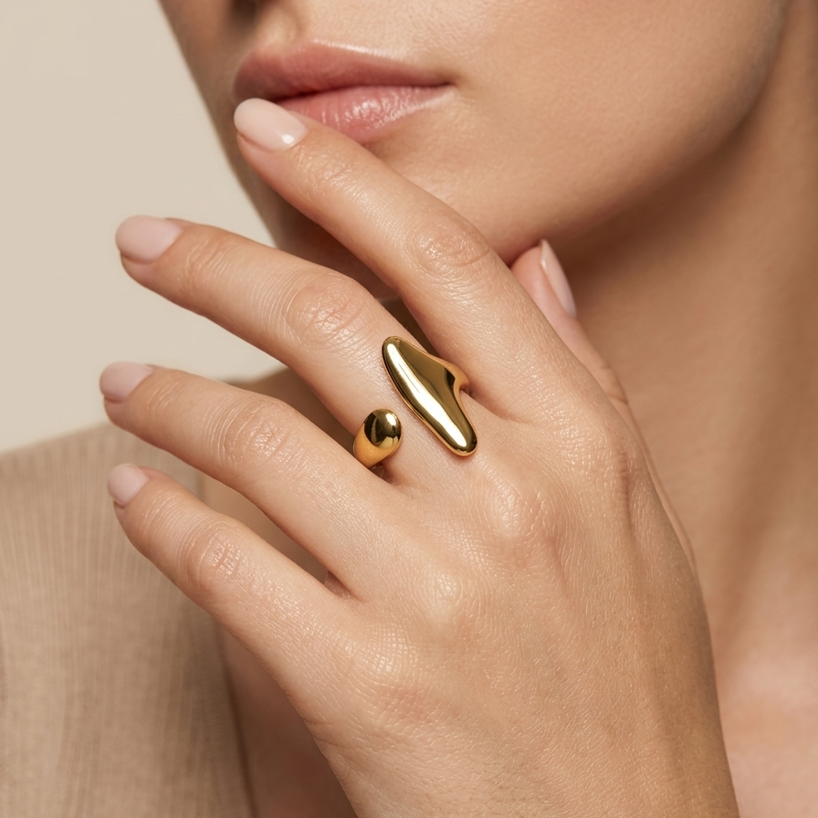 Close-up of a hand wearing a 18kt gold plated ring with a unique design, against a neutral background.