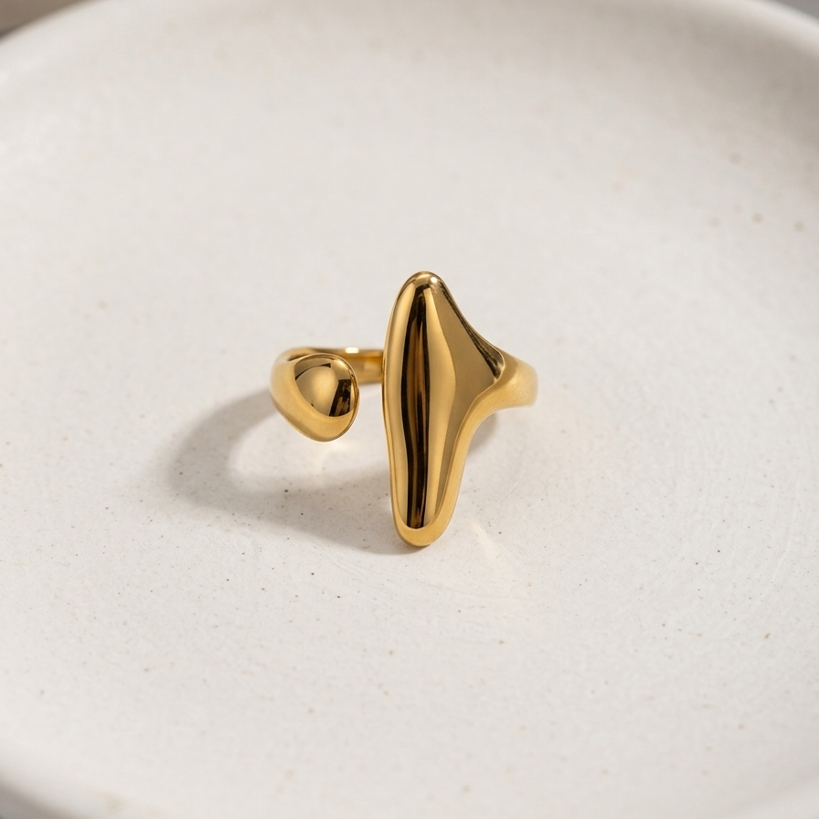 Abstract 18kt gold plated statement ring with elongated molten shape on white background.