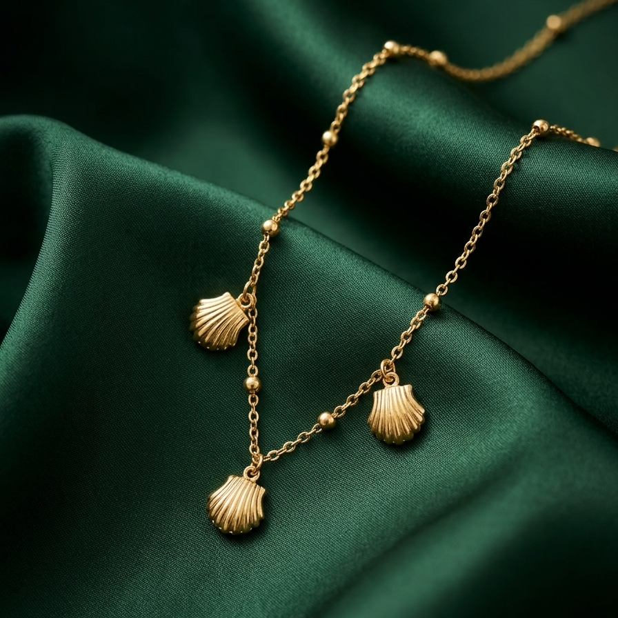 18kt gold plated shell charm necklace on a green fabric background.