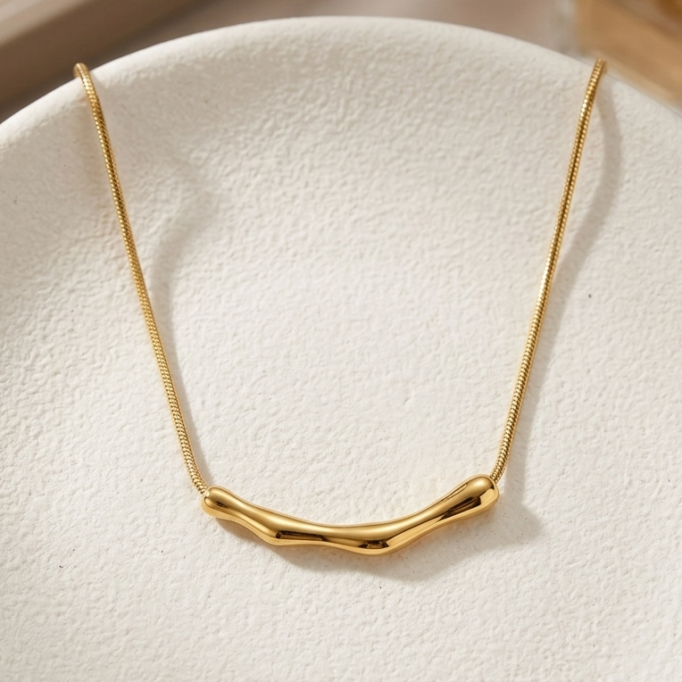 18kt gold plated bamboo bar necklace on a textured white surface.