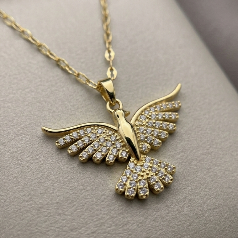 Close-up of 18kt gold plated necklace with a crystal bird pendant on a gray surface.