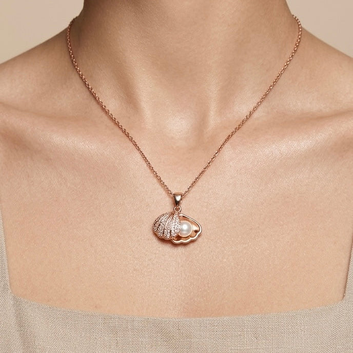 Rose gold necklace with a hidden pearl shell pendant worn by a person in a beige neutral outfit.