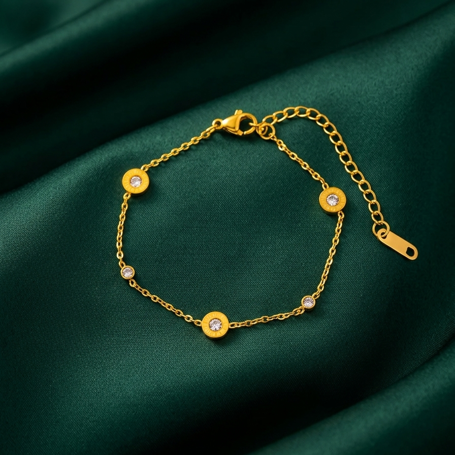 18kt gold plated, waterproof roman numeral station bracelet resting on smooth dark green fabric.