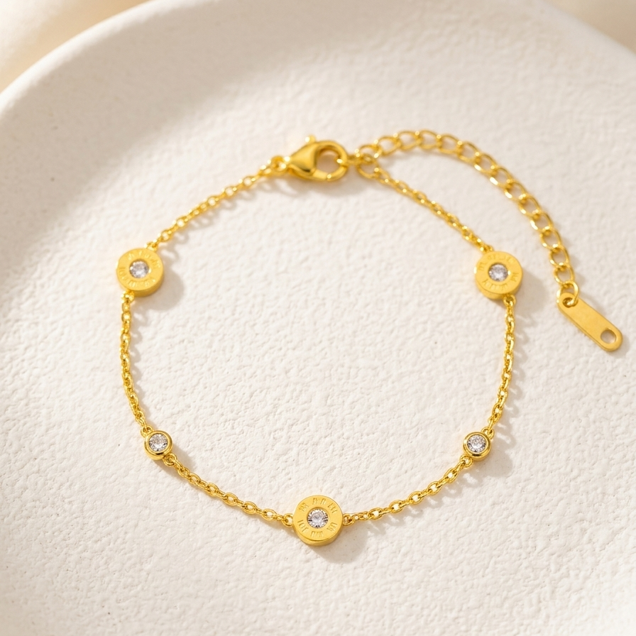 18kt gold plated, anti-tarnish chain bracelet with Roman numeral and crystal station charms on textured white plate.