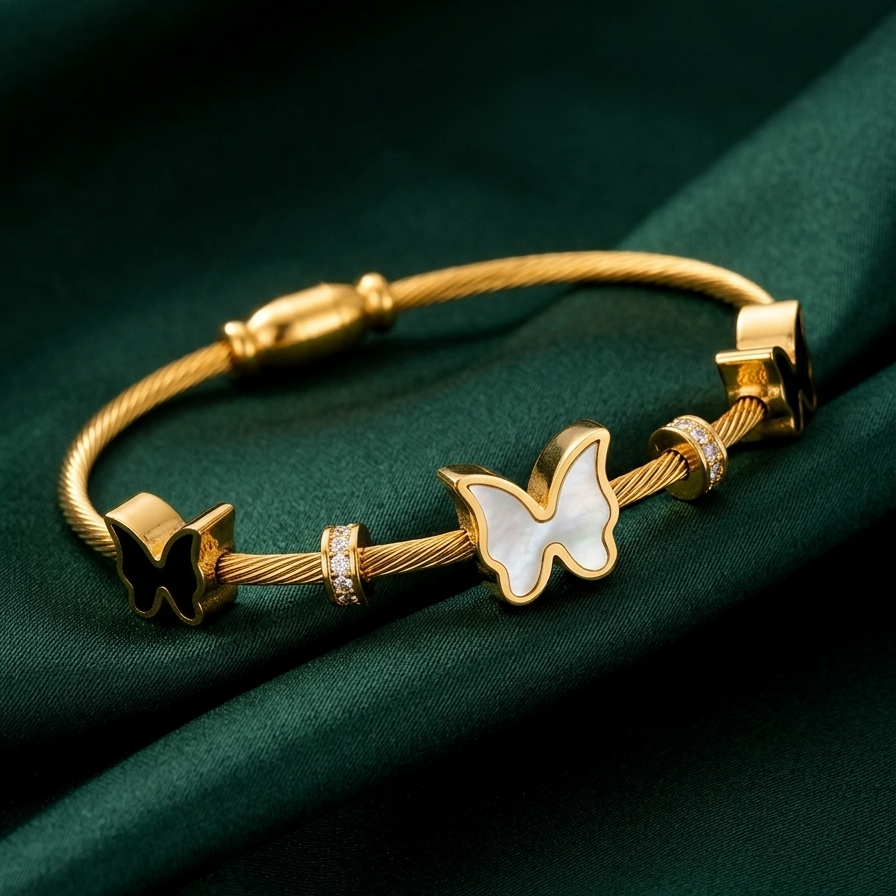 18kt gold plated cable wire magnetic bangle bracelet with black and white butterfly charms on smooth dark green cloth.