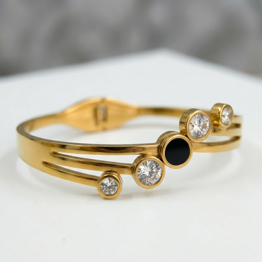 A close-up photography of 18kt gold plated, waterproof, the onyx crystal orbit bangle bracelet on off-white stone.