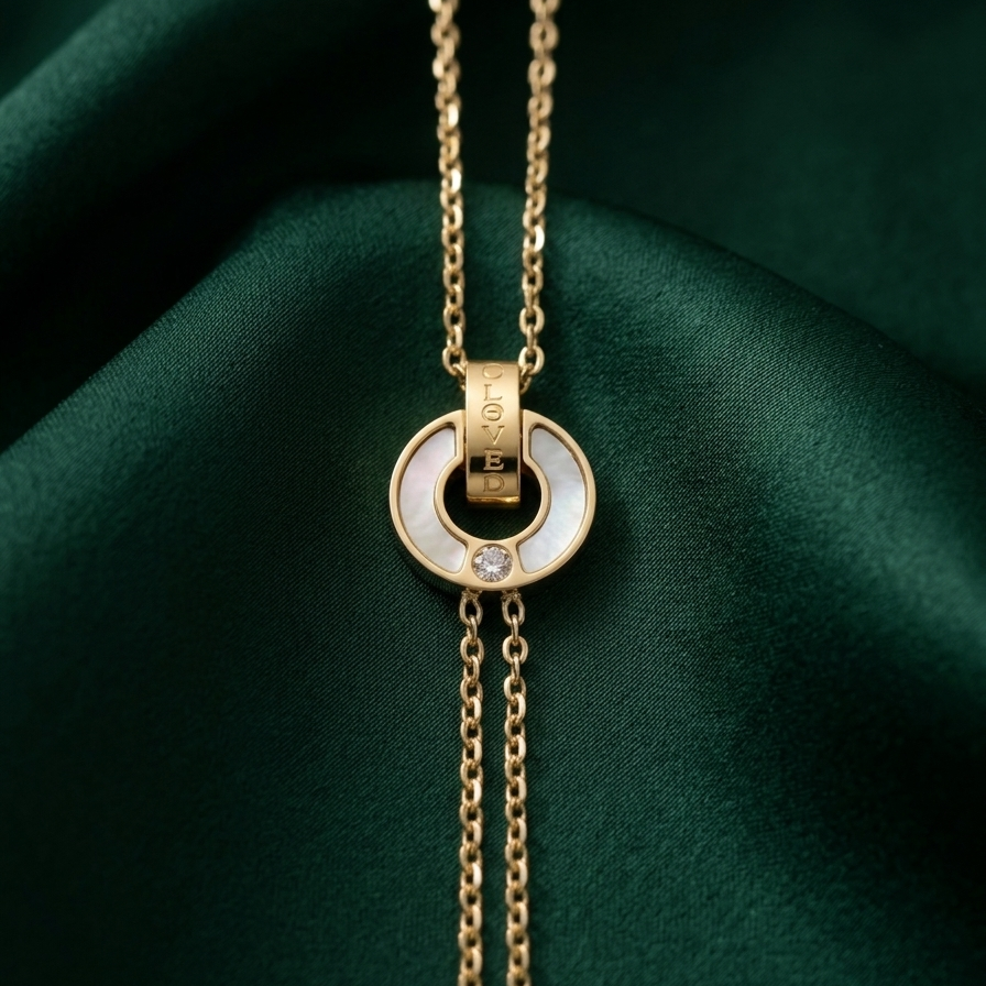 18kt gold plated, waterproof chain bracelet with interlocking circles, mother of pearl inlay and engraved "BELOVE" text resting on smooth dark green fabric.