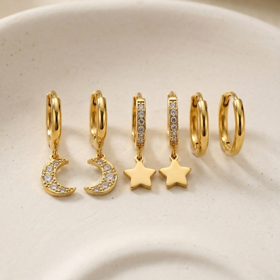 18kt gold plated celestial trio earring set lying on a off-white ceramic plate.