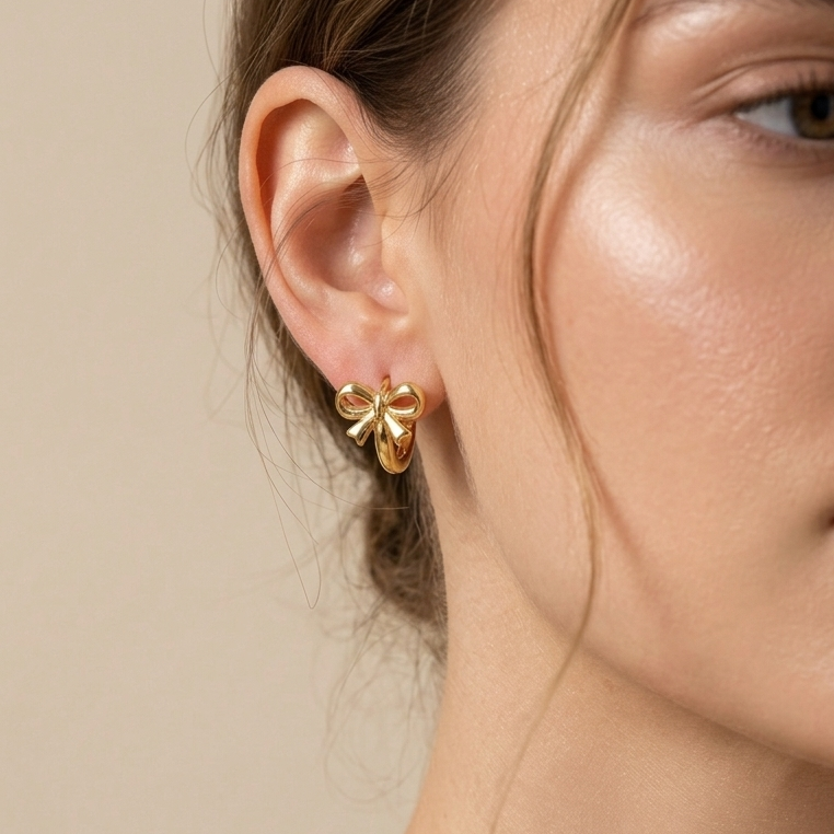 A woman model worn 18kt gold plated ribbon bow huggies on her ear.