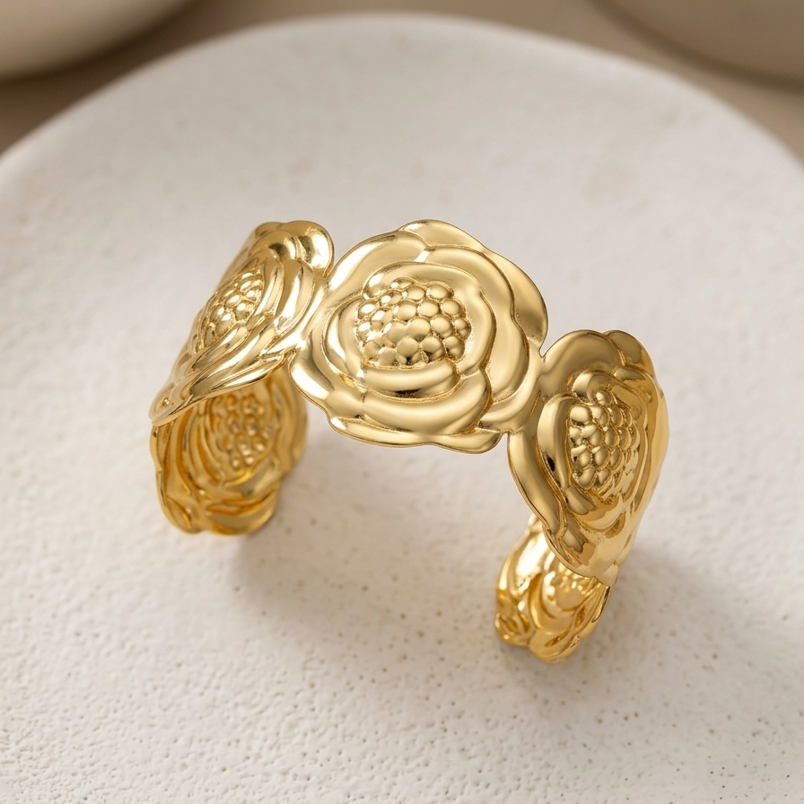 18kt gold plated, anti-tarnish wide cuff bracelet with sculpted camellia flower design on white stone against beige background.