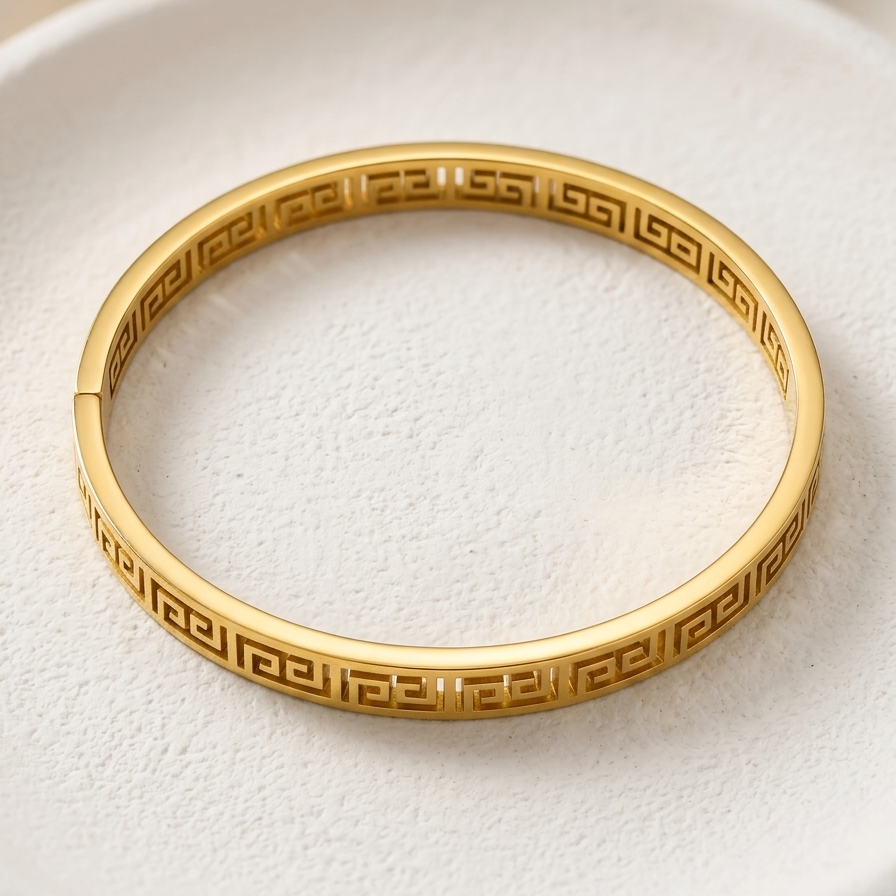 18kt gold plated, anti-tarnish greek key bangle bacelet resting on off-white plate.