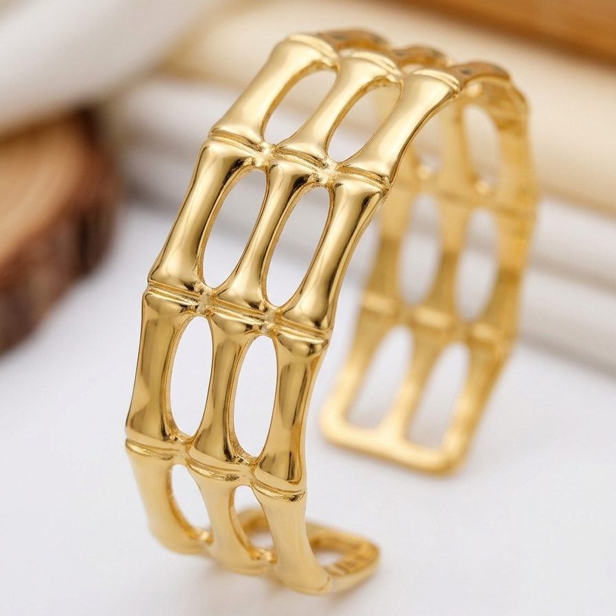 A close-up of 18kt gold plated, anti-tarnish gilded bamboo open cuff bracelet on beige background.