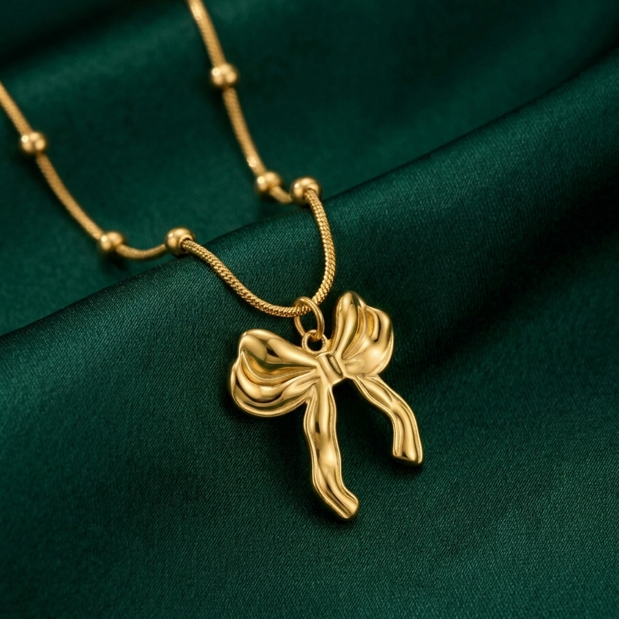 18kt gold plated 3D puffed bow pendant necklace on green fabric.