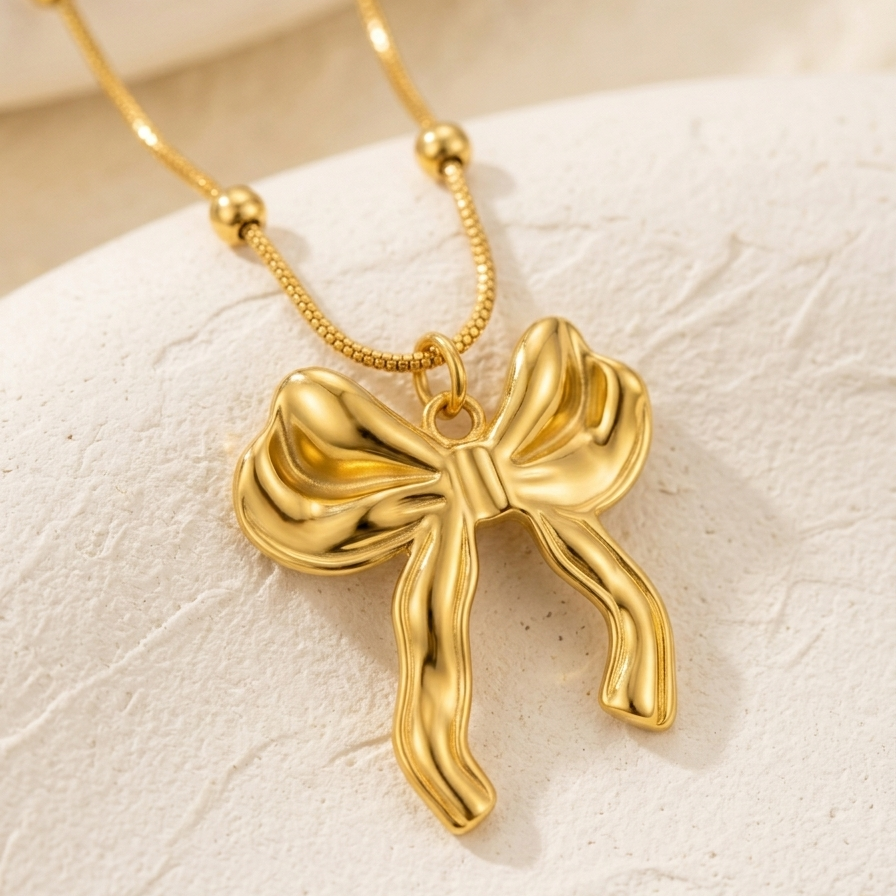 close-up photo of a 18kt gold plated 3D puffed bow necklace lying on off-white background.