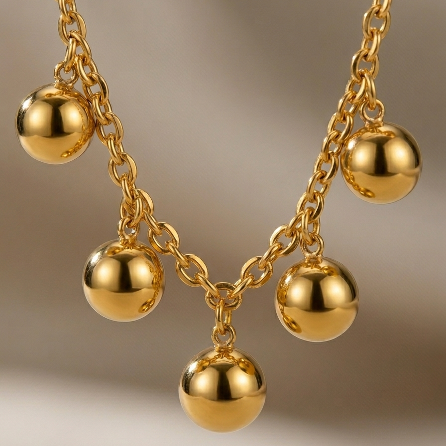 Close-up of a 18kt gold plated necklace with spherical beads on a neutral background.