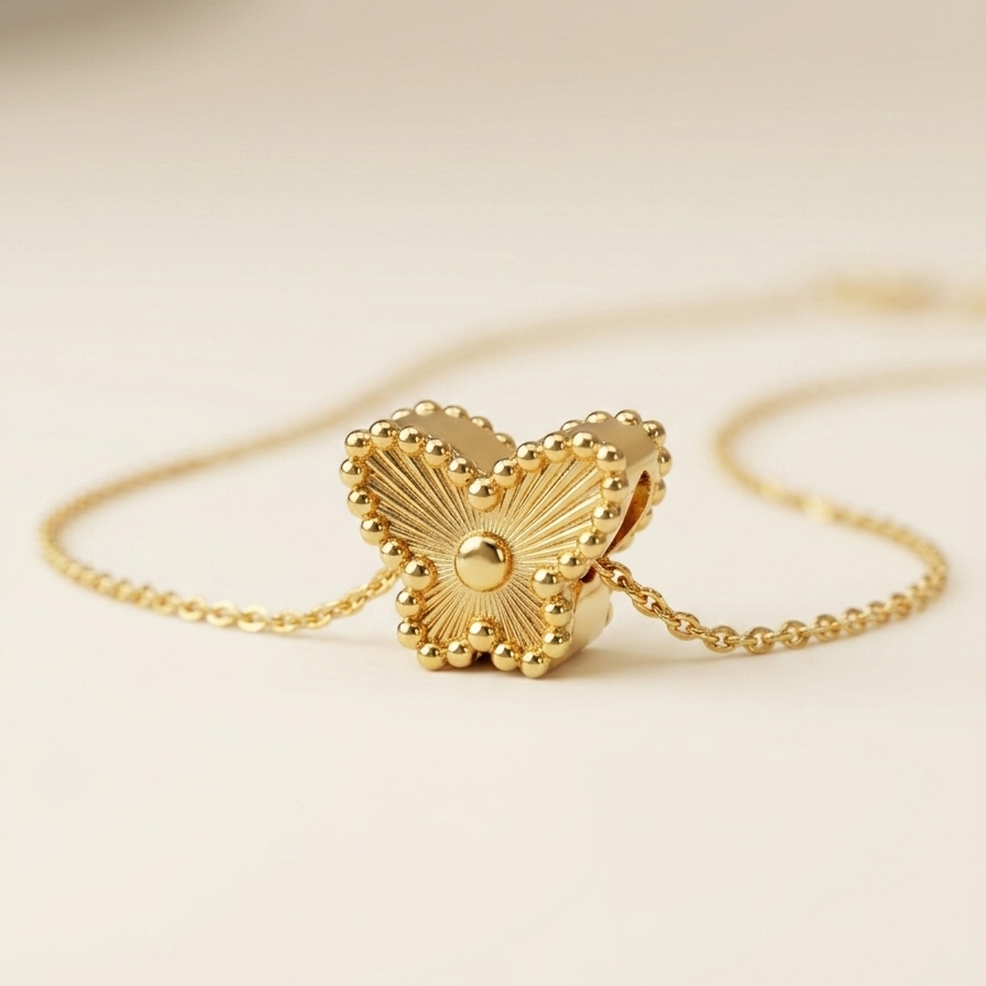 A close-up of 18kt gold plated butterfly necklace on a light beige background.