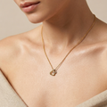 Gold necklace with a heart pendant worn by a person against a neutral background