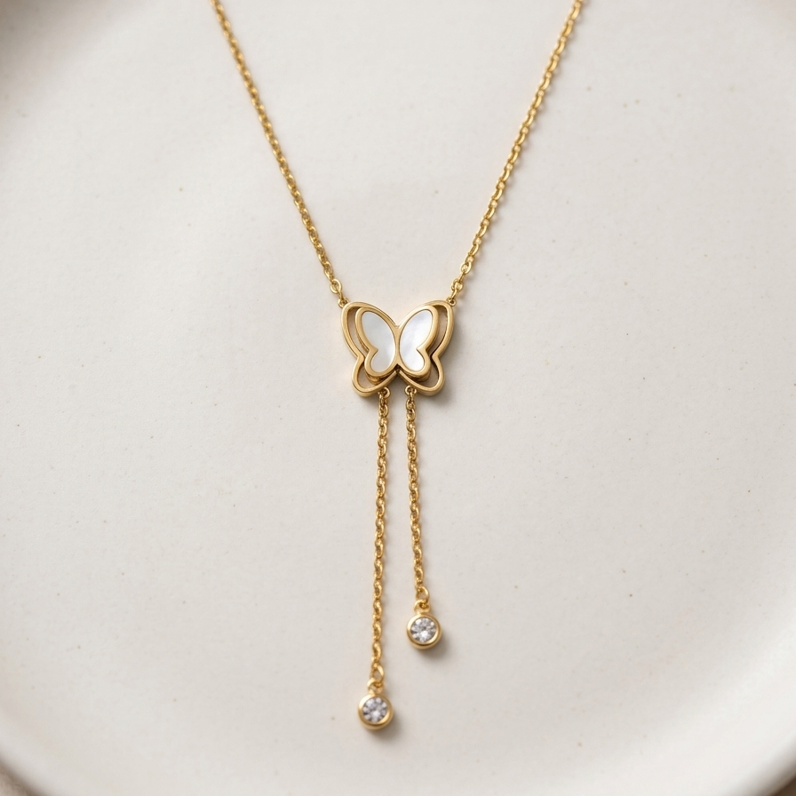 18kt gold plated butterfly necklace with dangling tassels lying on white texture surface.