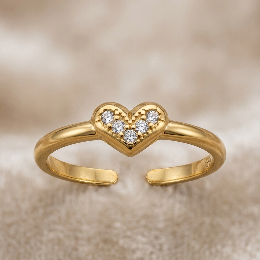 A gold adjustable ring with a small heart-shaped cluster of clear stones in the center, displayed on a soft beige textured background.