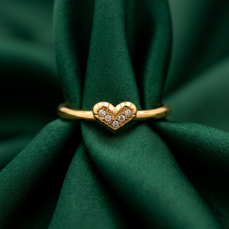 A gold heart-shaped ring with small clear stones, displayed on a dark green satin fabric background.