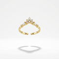 A gold ring with a split band and a small cluster of clear stones at the top, flanked by smaller side stones, shown on a light gray background with a soft shadow below.