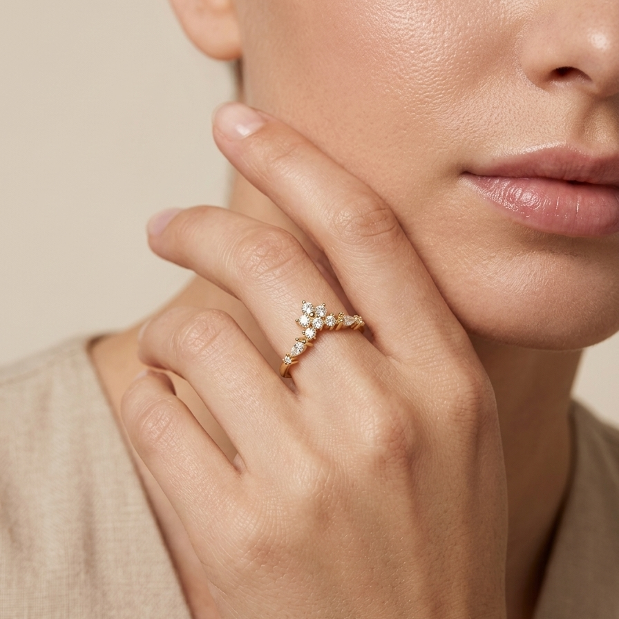A close-up lifestyle shot of a woman wearing a delicate gold ring with small clear stones on her finger, set against a soft beige background.