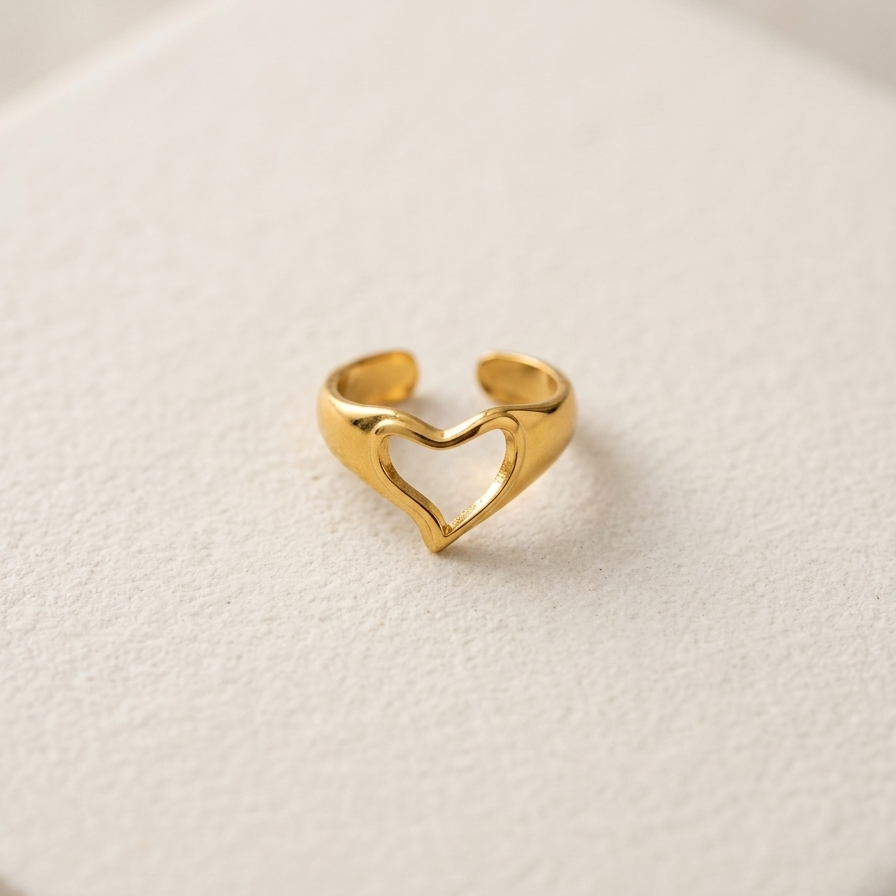 A gold open-heart adjustable ring displayed on a textured white surface.