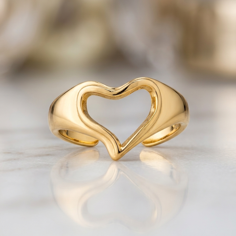 A polished gold ring with an open heart design, resting on a light marble surface with a soft, blurred background.