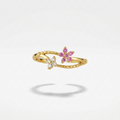 A delicate gold ring featuring two small flower motifs, one with pink gemstones and one with clear stones, set against a clean white background with a soft shadow.