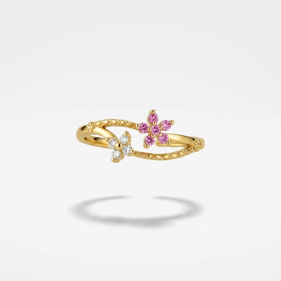 A delicate gold ring featuring two small flower motifs, one with pink gemstones and one with clear stones, set against a clean white background with a soft shadow.