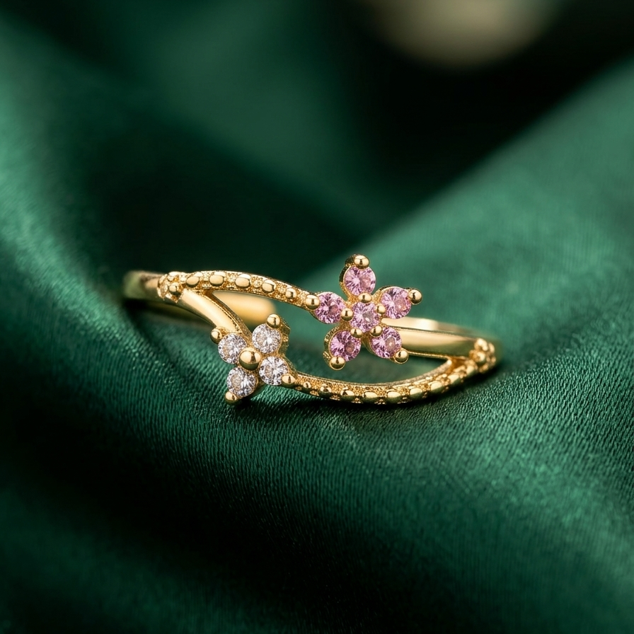 A gold ring with a floral design, featuring pink gemstones and small clear stones, resting on a dark green satin fabric background.