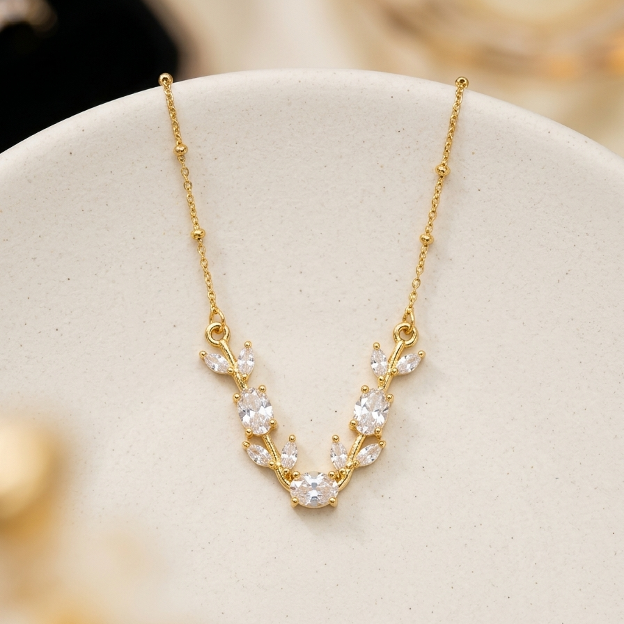 A delicate gold necklace with a V-shaped arrangement of clear, sparkling stones on a soft cream-colored display stand.
