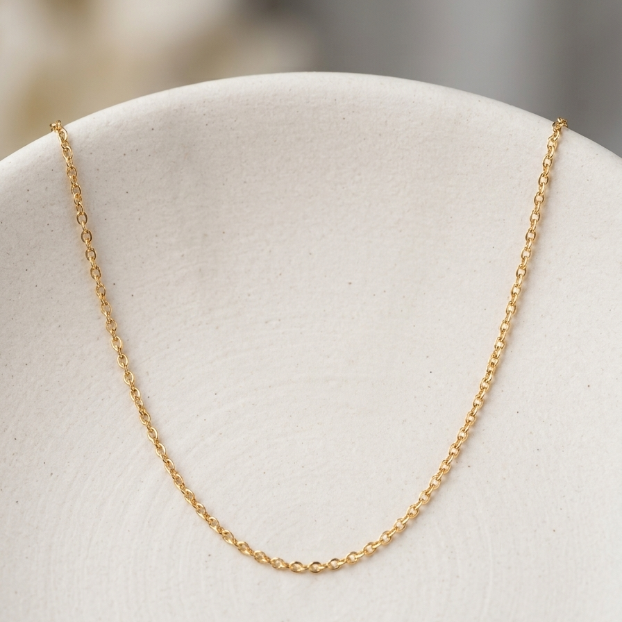 A delicate gold chain necklace draped over a textured off-white ceramic plate against a soft, blurred neutral background.
