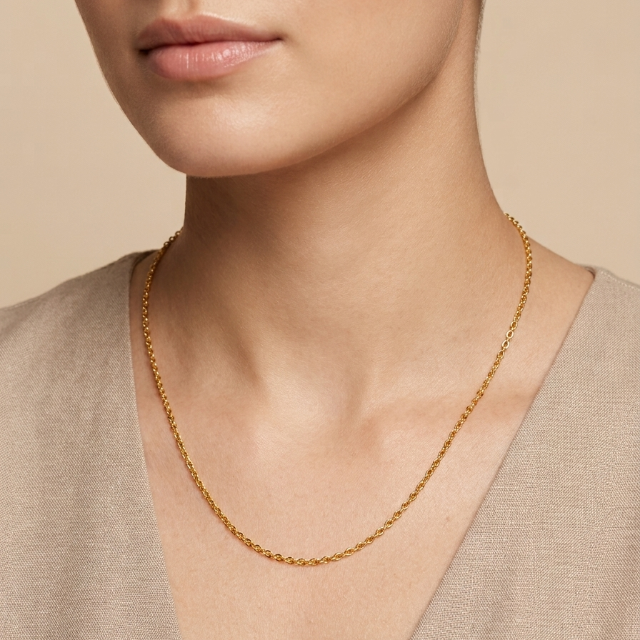 A close-up of a model wearing a delicate gold chain necklace with a twisted rope design, paired with a beige V-neck top against a warm beige background.