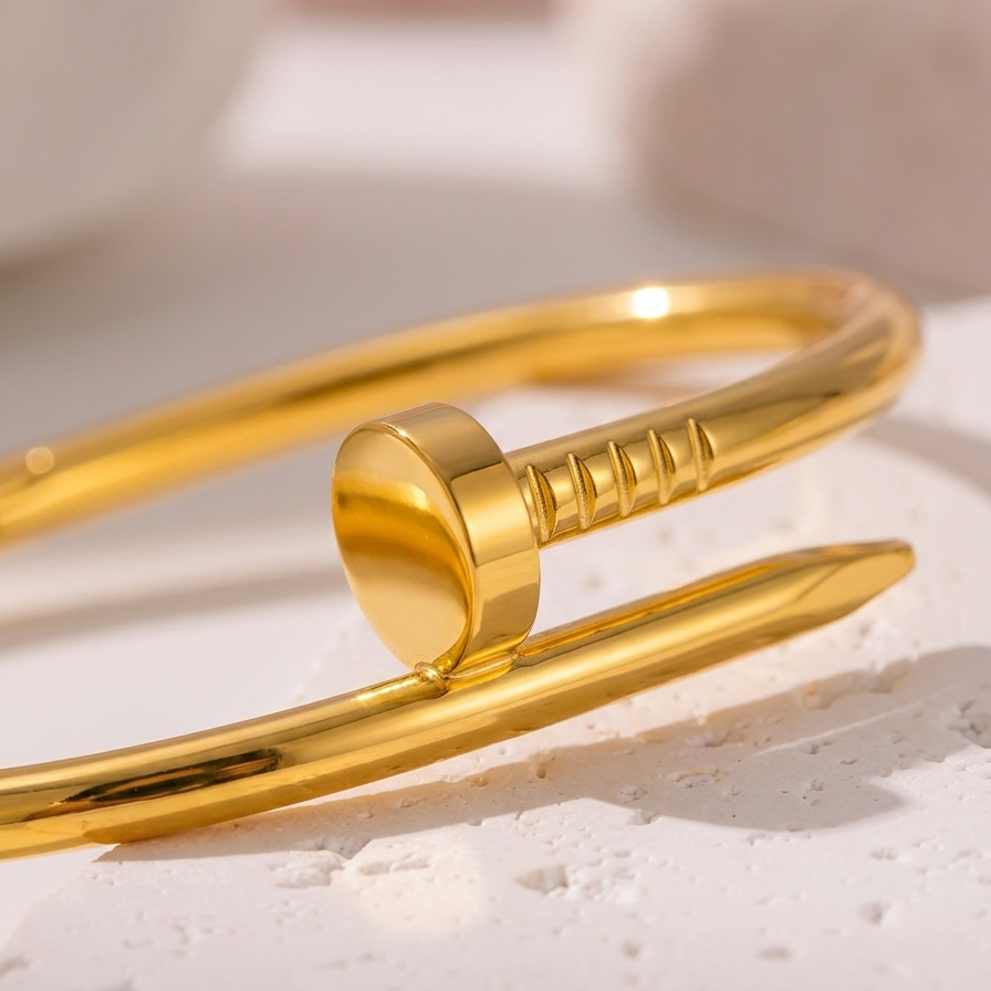 18kt gold plated iconic nail cuff bangle on a textured beige surface.