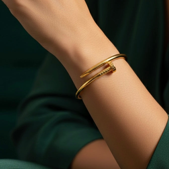 Gold bent nail design bangle bracelet on white stone prop.