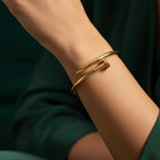 Gold bent nail design bangle bracelet on white stone prop.