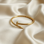 Gold bent nail design bangle bracelet on white stone prop.