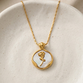 18k gold plated medallion necklace featuring a mother of pearl inlay and a raised golden rose motif in the center resting on a ceramic plate.