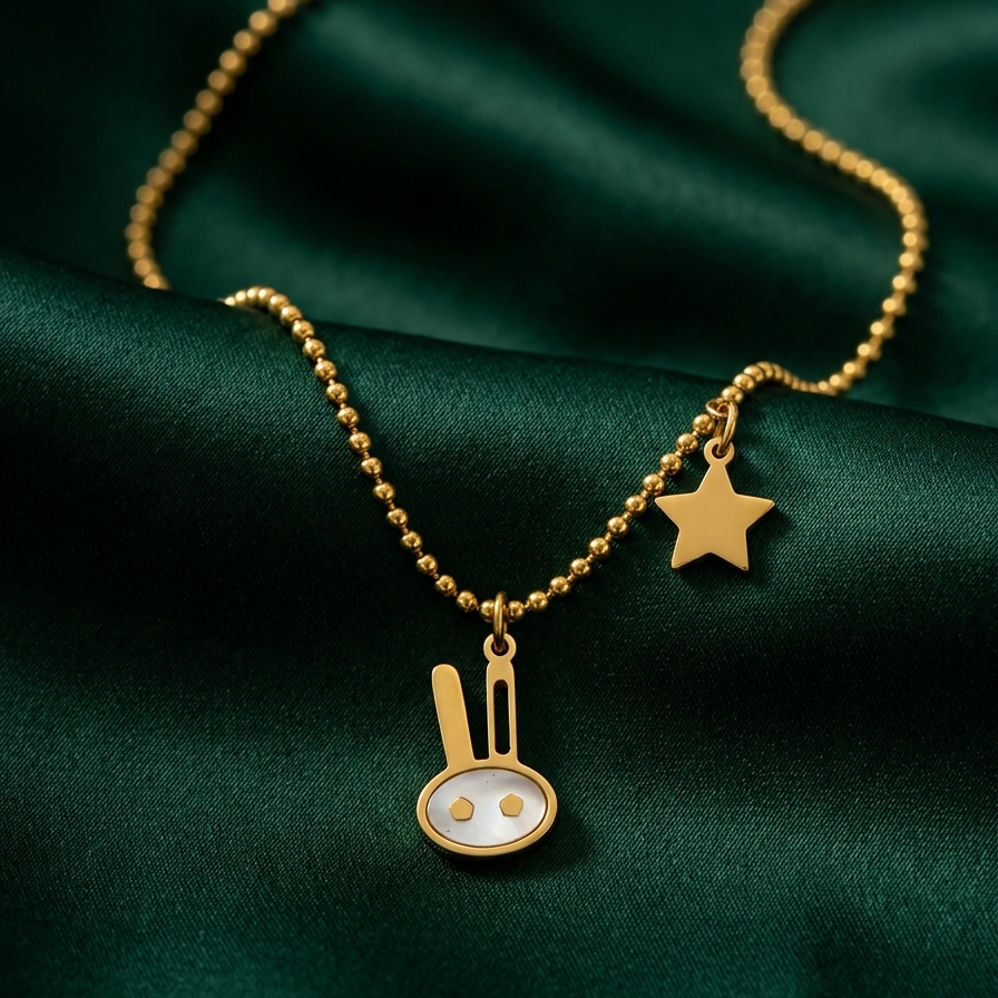 18k gold plated beaded chain necklace featuring a minimalist bunny charm with pearl inlay and a small golden star charm on a green fabric background