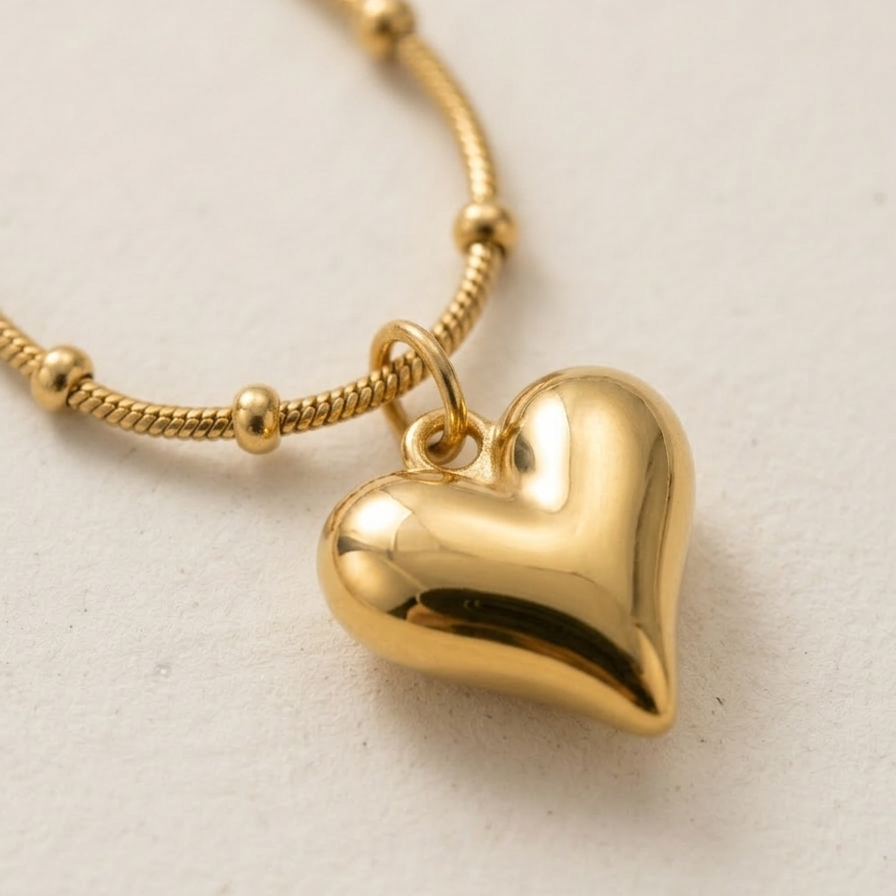 Close up of a 18k gold plated necklace featuring a smooth, 3D puffy heart pendant suspended on a delicate beaded satellite chain.