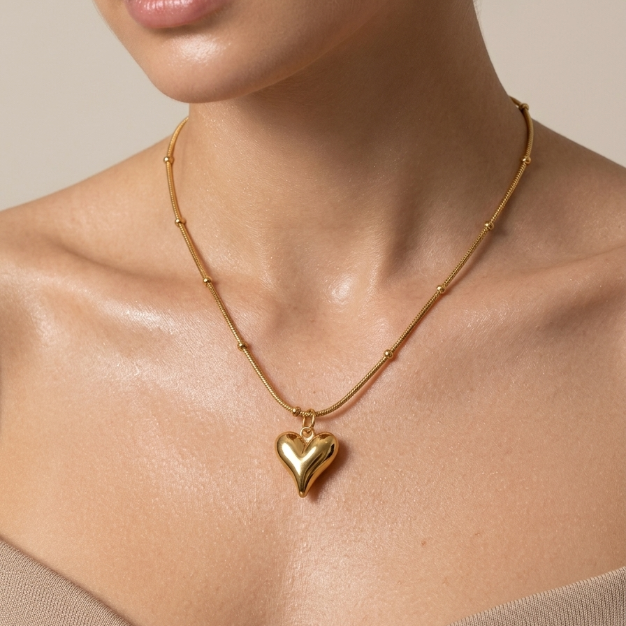 18k gold plated necklace featuring a smooth, 3D puffy heart pendant suspended on a delicate beaded satellite chain worn by a person on a neutral background